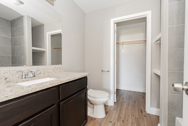 bathroom featuring a walk in closet, toilet, vanity, wood finished floors, and baseboards