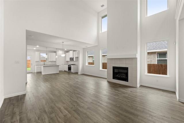279 Bright Alcove Ct, Lavon, TX 75166 - unfurnished living room with a high ceiling, dark wood-style flooring, a tiled fireplace, and baseboards