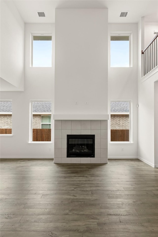 279 Bright Alcove Ct, Lavon, TX 75166 - unfurnished living room featuring a high ceiling, a tiled fireplace, wood finished floors, and baseboards