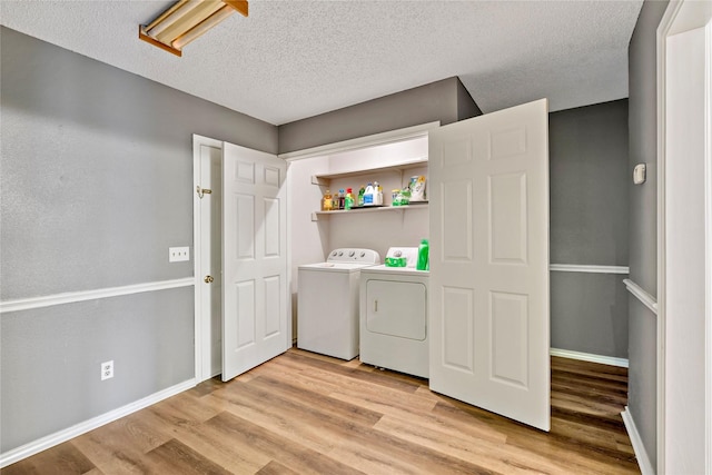 clothes washing area featuring a textured ceiling, separate washer and dryer, light wood-type flooring, laundry area, and baseboards