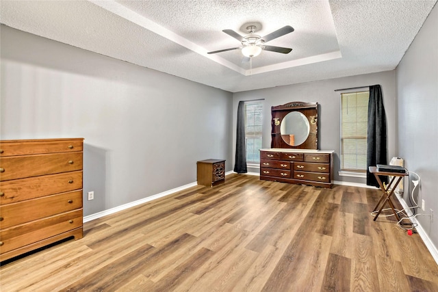 bedroom with a textured ceiling, a raised ceiling, light wood-style flooring, and baseboards