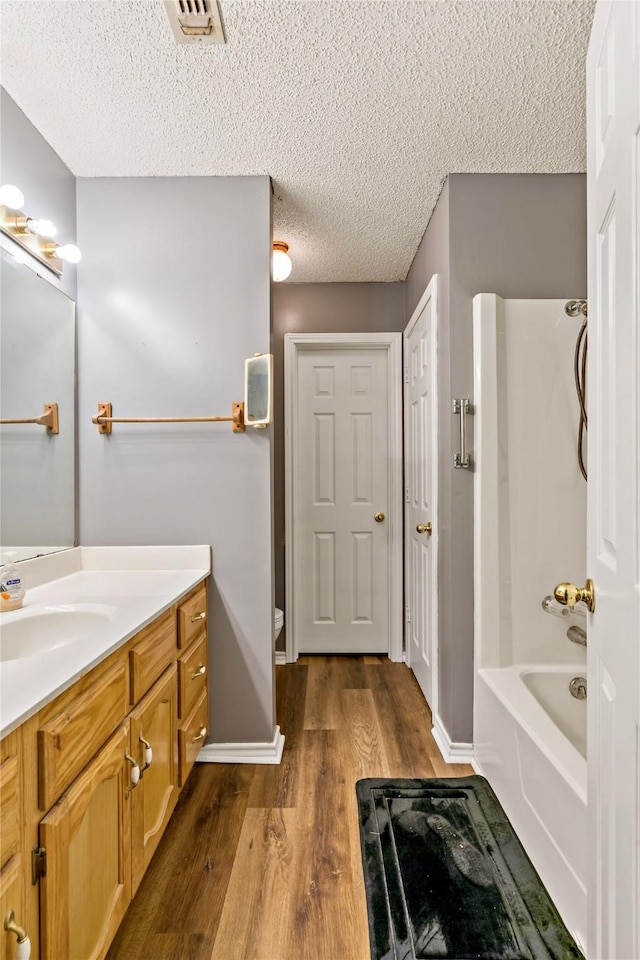 full bathroom featuring a textured ceiling, wood finished floors, visible vents, vanity, and tub / shower combination