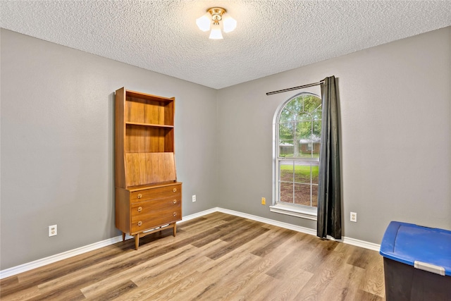 spare room featuring light wood-style flooring, baseboards, and a textured ceiling