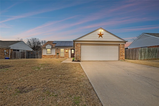 view of front facade featuring roof mounted solar panels, brick siding, driveway, and fence