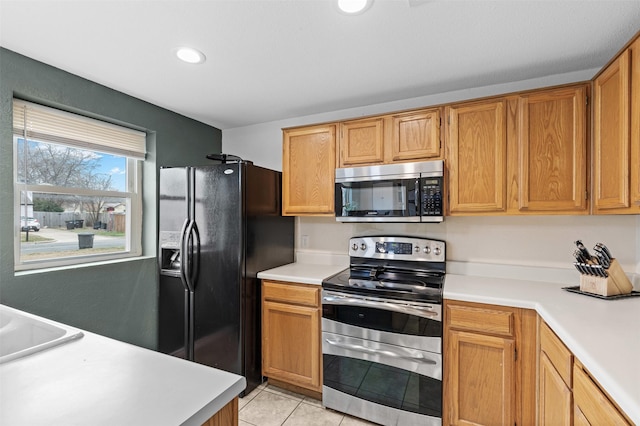 kitchen featuring light tile patterned floors, light countertops, appliances with stainless steel finishes, and brown cabinetry