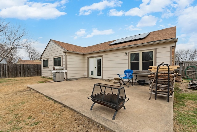 back of property featuring a fenced backyard, a fire pit, french doors, roof mounted solar panels, and a patio area