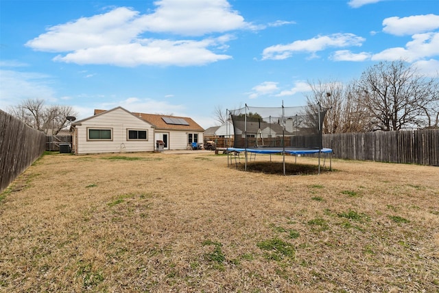 rear view of house with a trampoline, a fenced backyard, a yard, and central AC