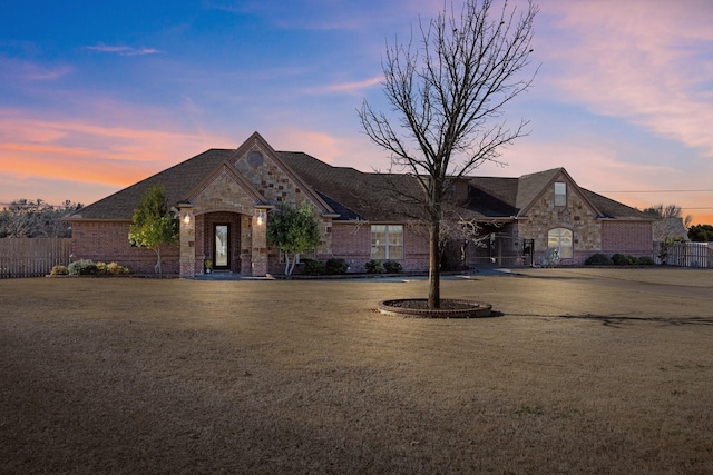 french country inspired facade featuring stone siding, a front lawn, fence, and brick siding