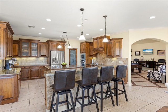 kitchen featuring arched walkways, stainless steel appliances, light tile patterned flooring, and brown cabinets