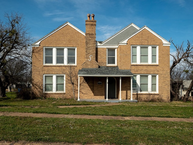 view of front facade with brick siding, a chimney, and a front yard