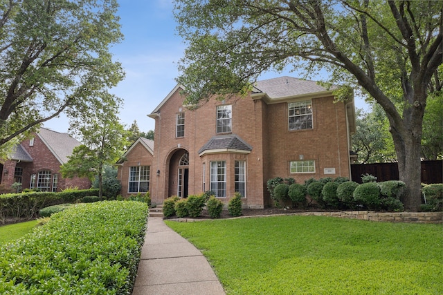 traditional home with a shingled roof, brick siding, fence, and a front lawn