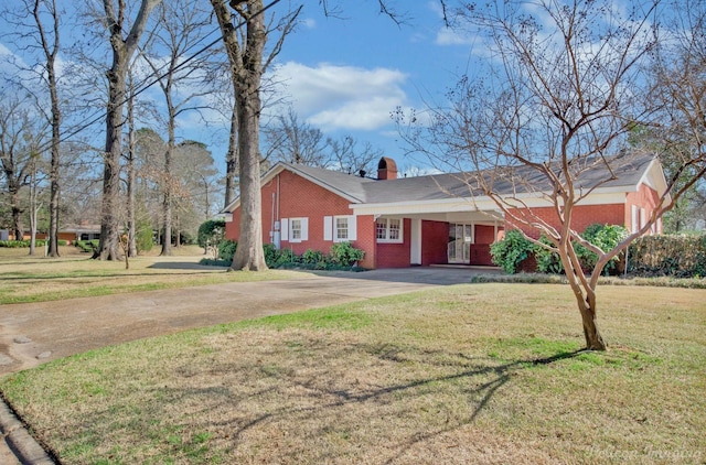 view of front of home with driveway, brick siding, a chimney, and a front yard