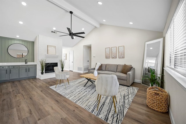 living area featuring a brick fireplace, vaulted ceiling with beams, baseboards, recessed lighting, and wood finished floors