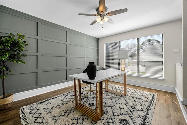 home office featuring a decorative wall, baseboards, a ceiling fan, and wood finished floors