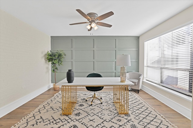 office featuring light wood finished floors, brick wall, a ceiling fan, and a decorative wall