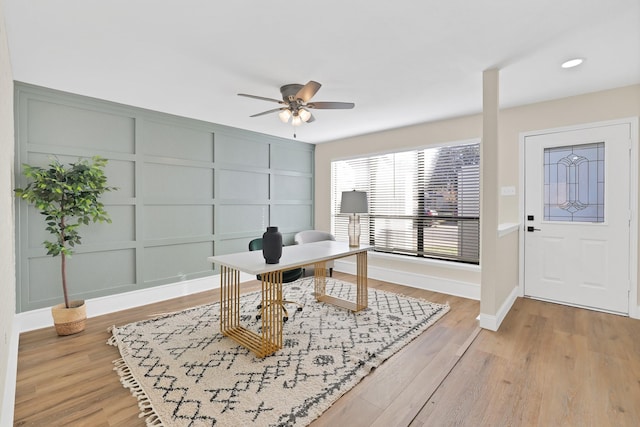 home office featuring baseboards, a decorative wall, light wood finished floors, and ceiling fan