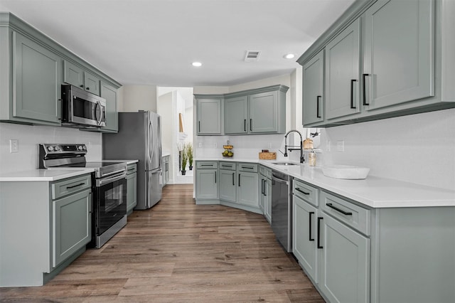 kitchen with wood finished floors, recessed lighting, a sink, light countertops, and appliances with stainless steel finishes