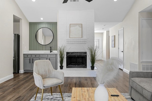 living room featuring dark wood-style floors, a fireplace, visible vents, and baseboards