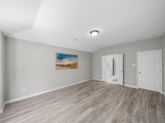 spare room with lofted ceiling, visible vents, light wood-style flooring, and baseboards