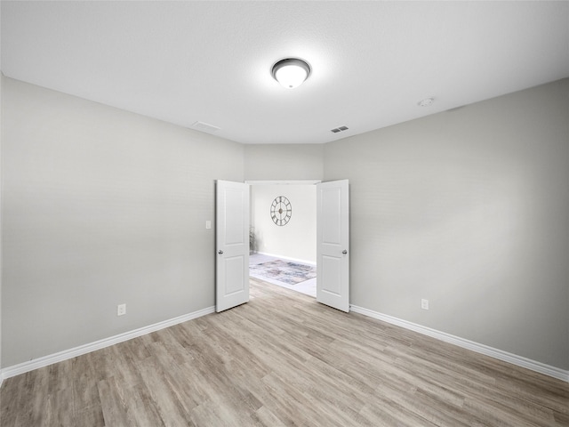 unfurnished room featuring light wood-type flooring, visible vents, and baseboards