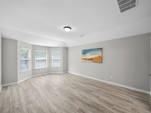 spare room featuring light wood finished floors, visible vents, and baseboards