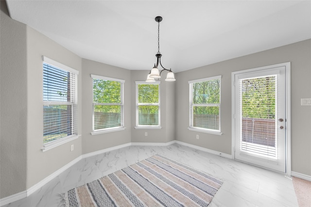 unfurnished dining area featuring a chandelier, marble finish floor, and baseboards