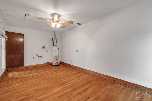 unfurnished room featuring gas water heater, light wood finished floors, visible vents, a ceiling fan, and baseboards