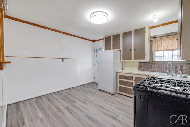 kitchen with a sink, light countertops, ornamental molding, freestanding refrigerator, and light wood finished floors