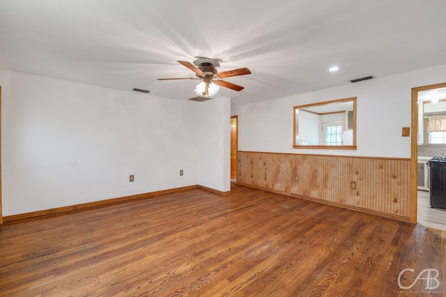 spare room with a wainscoted wall, ceiling fan, dark wood-style flooring, and visible vents