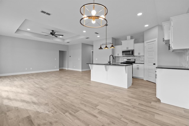 kitchen featuring dark countertops, an island with sink, appliances with stainless steel finishes, decorative light fixtures, and white cabinetry