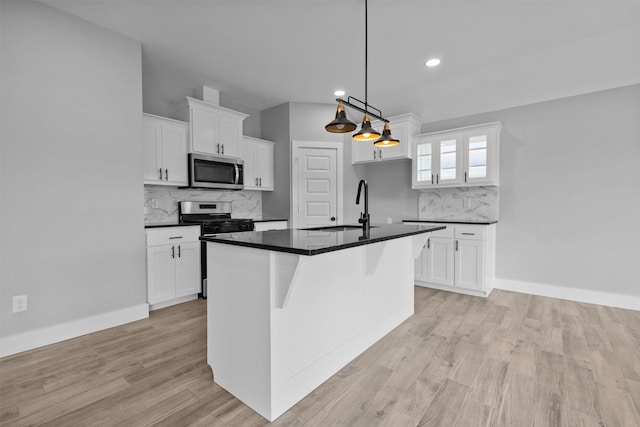 kitchen featuring dark countertops, appliances with stainless steel finishes, hanging light fixtures, white cabinetry, and a sink