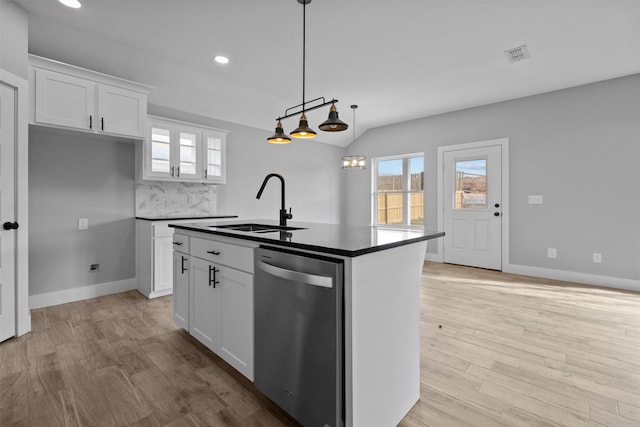 kitchen with dark countertops, white cabinets, an island with sink, and stainless steel dishwasher