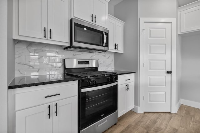 kitchen with light wood finished floors, decorative backsplash, appliances with stainless steel finishes, dark stone countertops, and white cabinetry