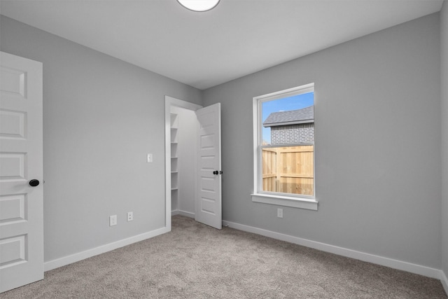 unfurnished bedroom with light carpet, a spacious closet, and baseboards