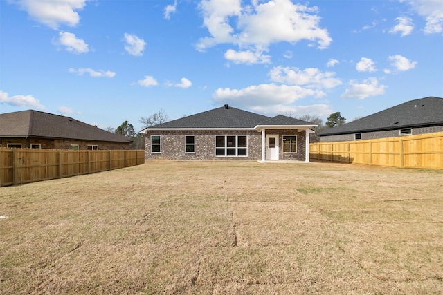 rear view of house featuring a fenced backyard, a lawn, and brick siding