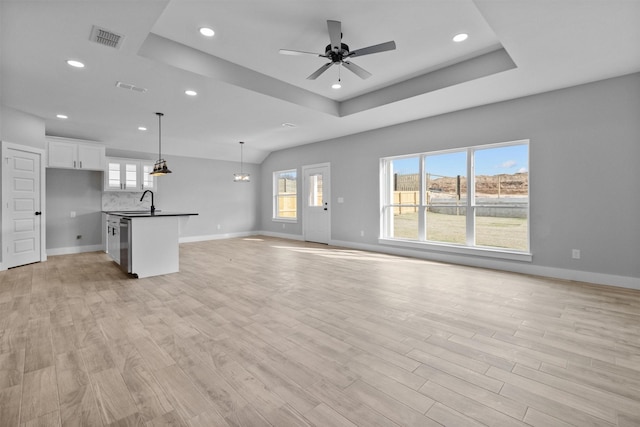 unfurnished living room with light wood-style floors, a raised ceiling, and visible vents