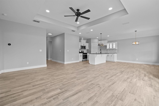 unfurnished living room featuring a tray ceiling, a ceiling fan, visible vents, and light wood-style floors