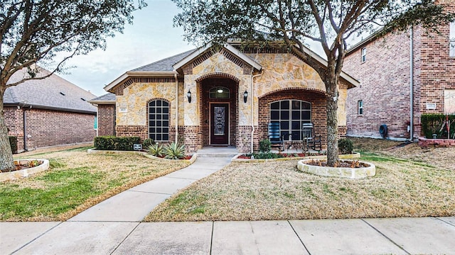 french country style house with stone siding, brick siding, and a front yard