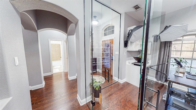 hall with arched walkways, dark wood finished floors, visible vents, and baseboards