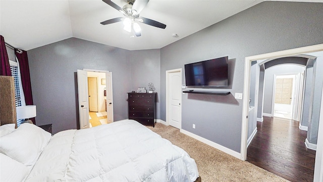 bedroom with baseboards, arched walkways, ensuite bath, ceiling fan, and vaulted ceiling