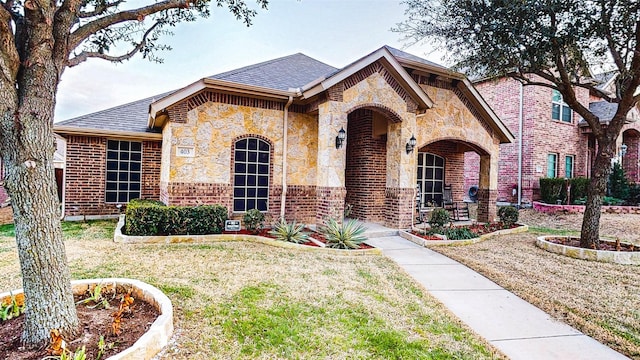 view of front of home featuring stone siding, a shingled roof, a front yard, and brick siding