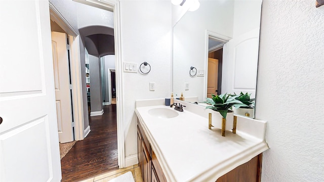 bathroom with a textured wall, baseboards, wood finished floors, and vanity