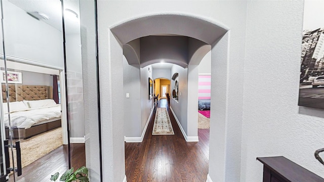 hall with dark wood-style floors, arched walkways, a textured wall, and baseboards