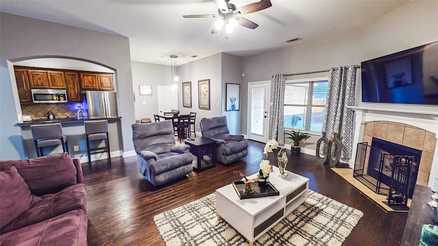 living room featuring baseboards, visible vents, dark wood-type flooring, and a tile fireplace