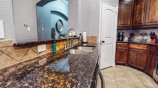 kitchen featuring light tile patterned floors, backsplash, dark stone countertops, and a sink