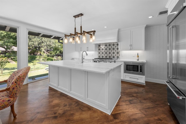 kitchen with premium range hood, white cabinetry, appliances with stainless steel finishes, an island with sink, and pendant lighting