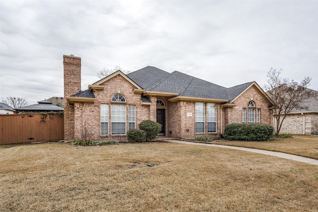 ranch-style house with brick siding, roof with shingles, fence, and a front yard