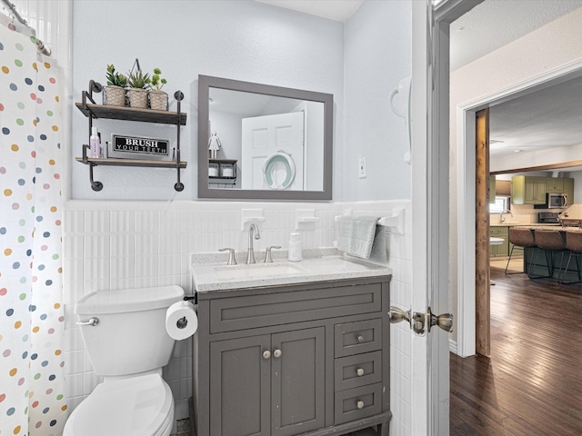 bathroom with tile walls, toilet, wainscoting, vanity, and wood finished floors