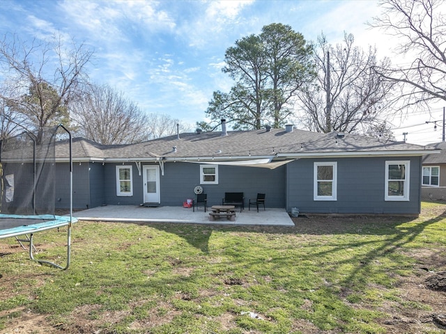 back of property with a trampoline, an outdoor fire pit, a patio area, and a lawn