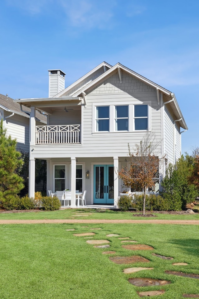 back of property featuring a chimney, a lawn, a balcony, and french doors